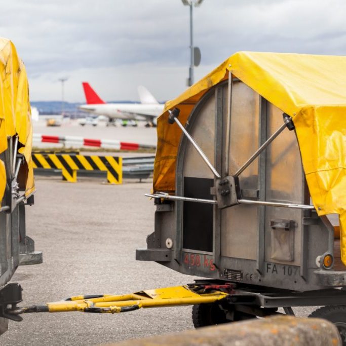 Trolleys loaded with luggage at an airport standing on the tarmac under yellow tarpaulins waiting to be loaded on an airplane